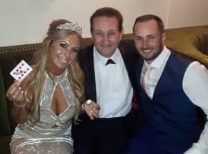 The magician Andy sitting with the bride and groom. The bride is holding a keepsake from their wedding magic performance.